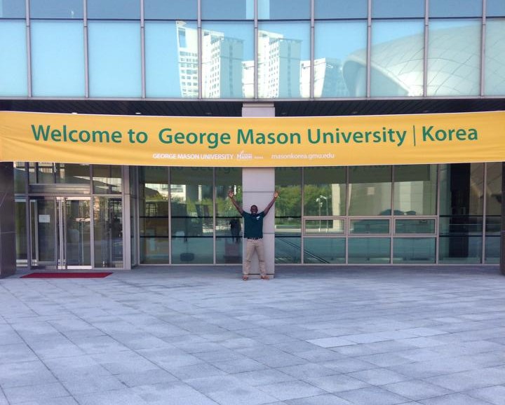 Tijani Musa poses in front of welcome sign at Mason Korea. 